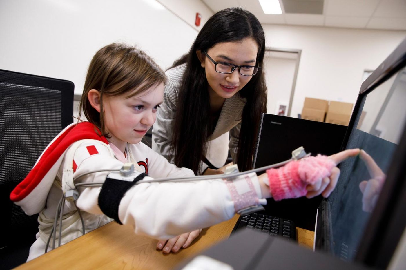 Di Wu directs a volunteer as she touches images on a screen using a device designed to track miniscule fluctuation in the arm's movement. Credit: James Brosher, Indiana University