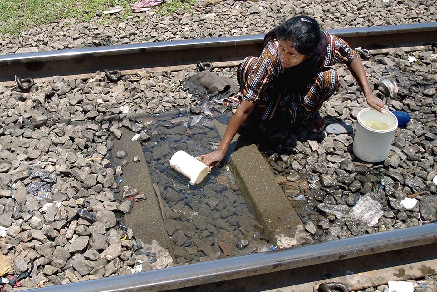 A slum dweller keeps an eye open fro trains as she collects water for drinking from a puddle in between railway tracks in Mumbai. Photo: Reuters