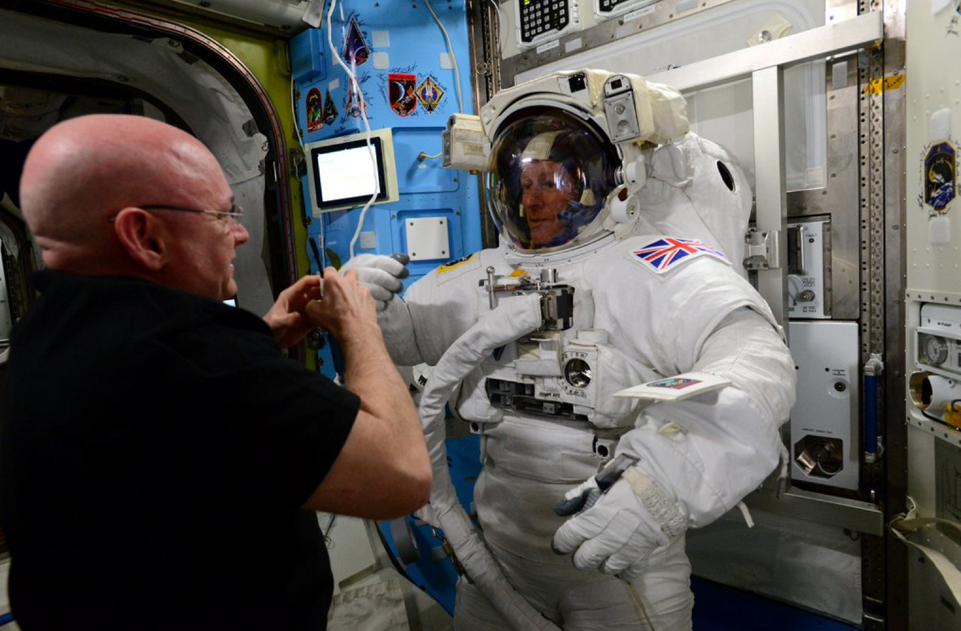 ESA's Tim Peake tries on his space suit with the help of Scott Kelly.