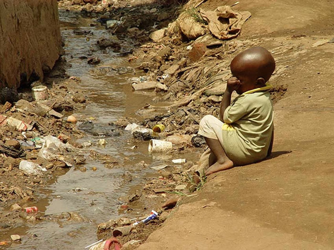 Child next to open sewer in slum in Kampala, Uganda, at risk of diarrhea and stunted growth