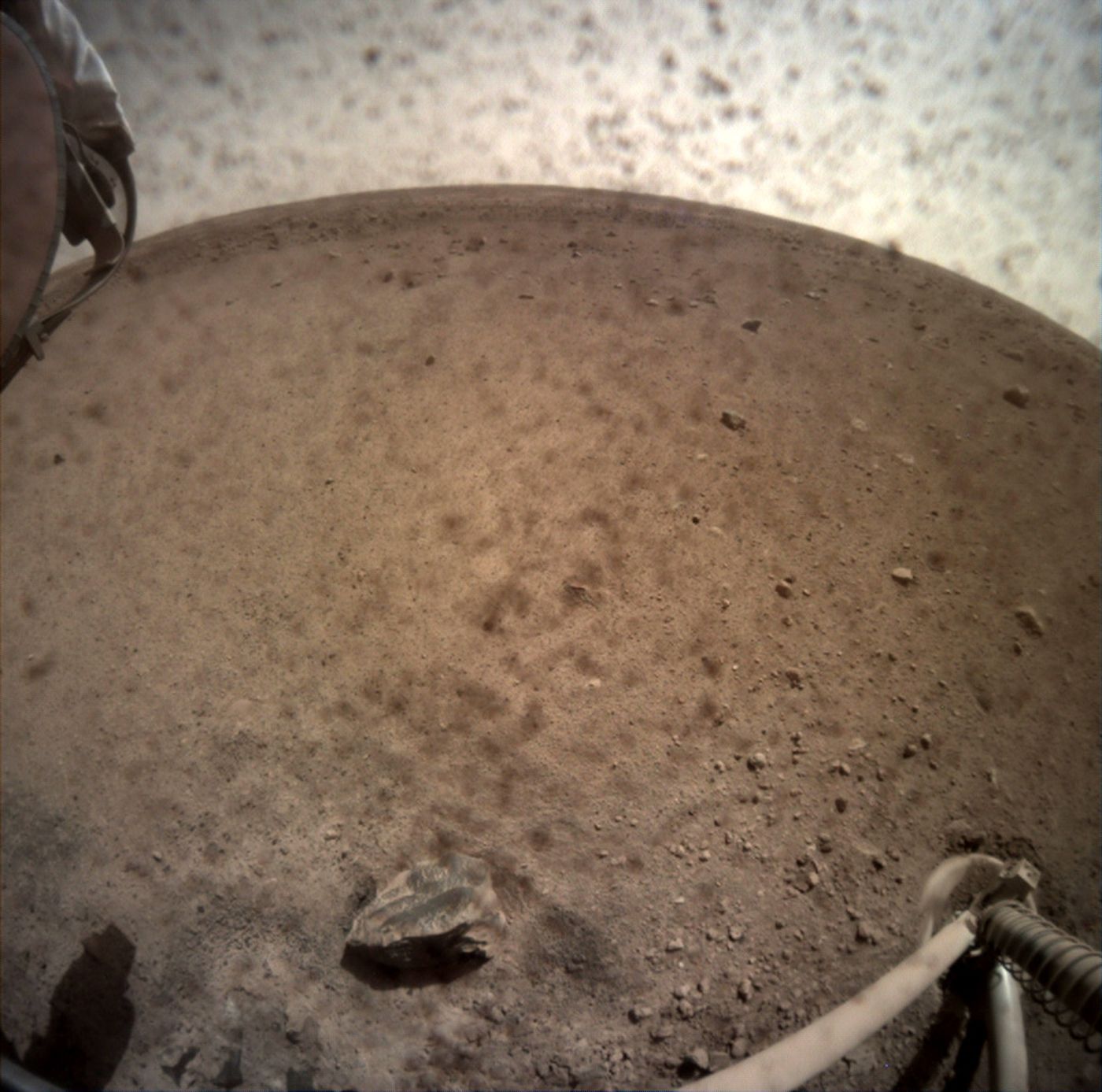 A dusty photograph showing off InSight's surroundings. One of the lander's feet is visible in the frame.