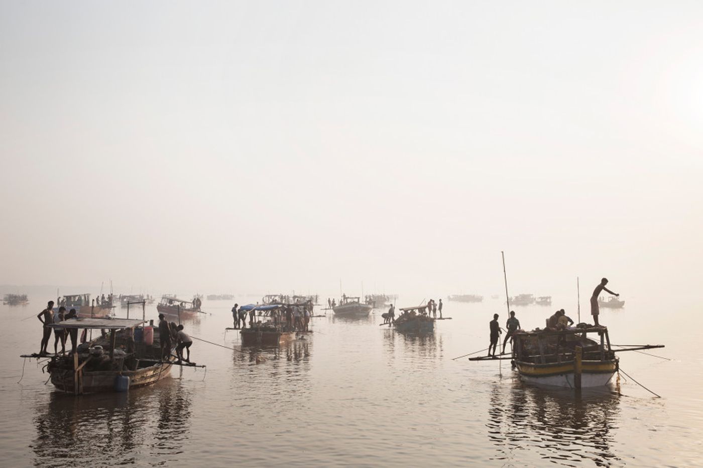 Sanding mining boats work illegally on the Thane Creek in Maharashtra, India. Workers dive to the bottom with a metal bucket to scoop sand; the boat crew hauls it to the surface.